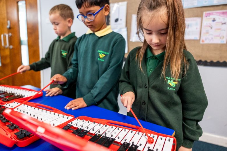Three small children play a xylophone