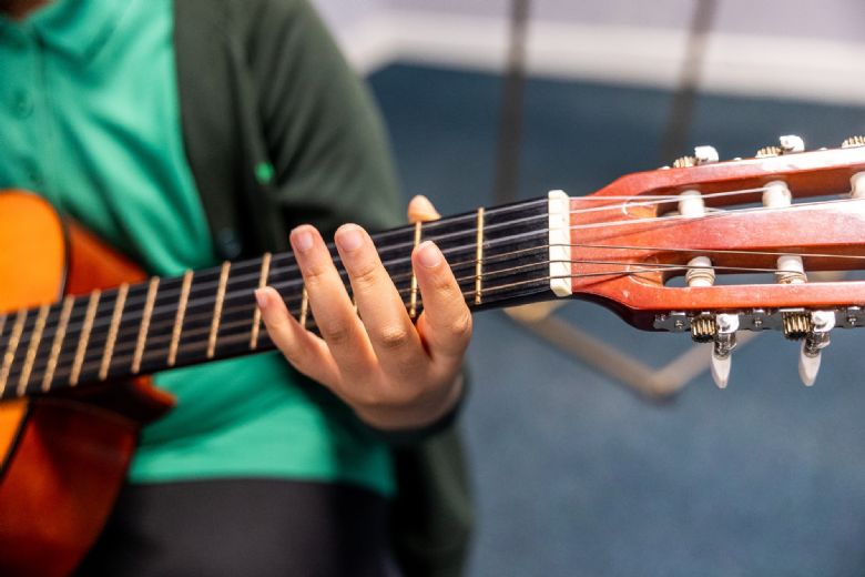 A close up of a hand making chords on the neck of a guitar