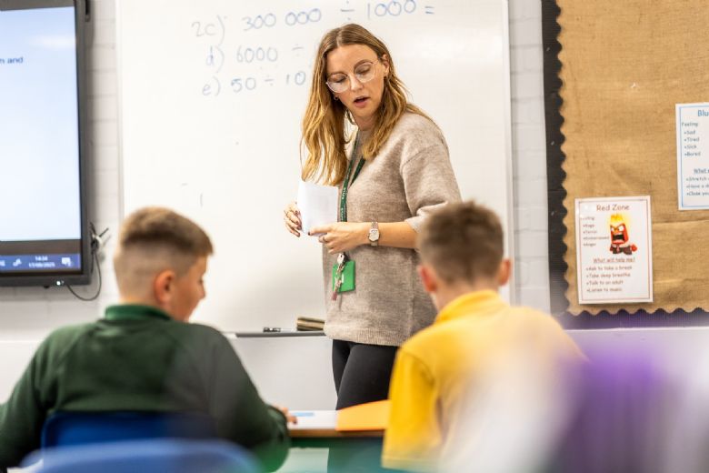 Picture of a female teacher showing pupils maths sums on a whiteboard