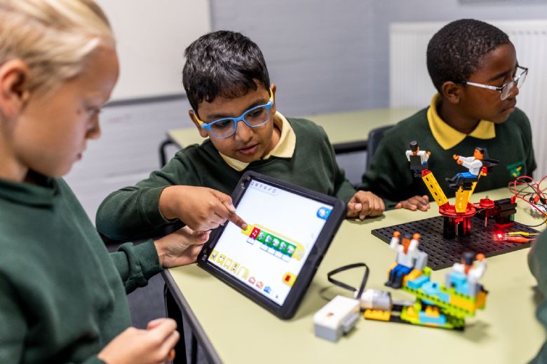 A group of children look at a tablet device  that is controlling robots